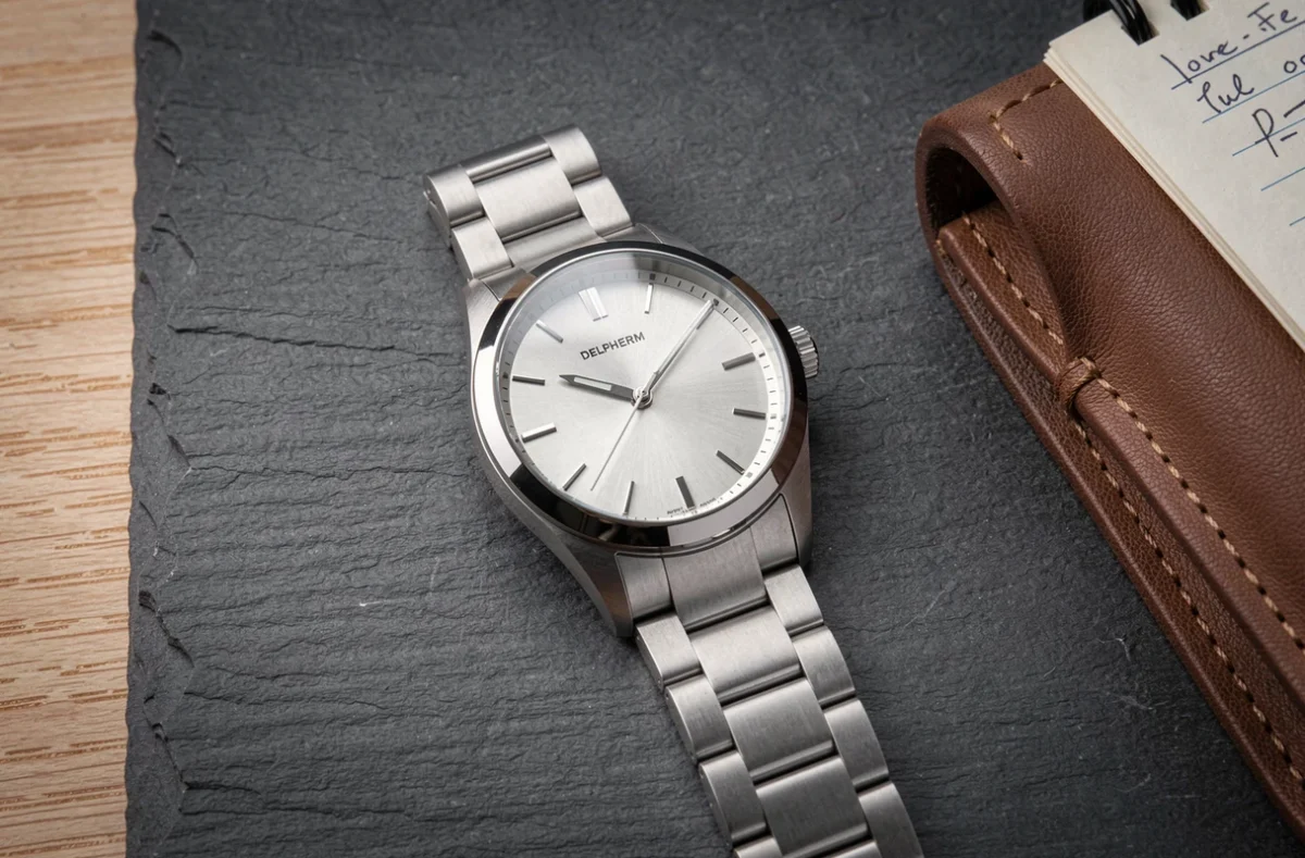 Gros plan détaillé d'une montre Delpherm posée sur ardoise avec carnet de notes, illustrant un test qualité-prix approfondi