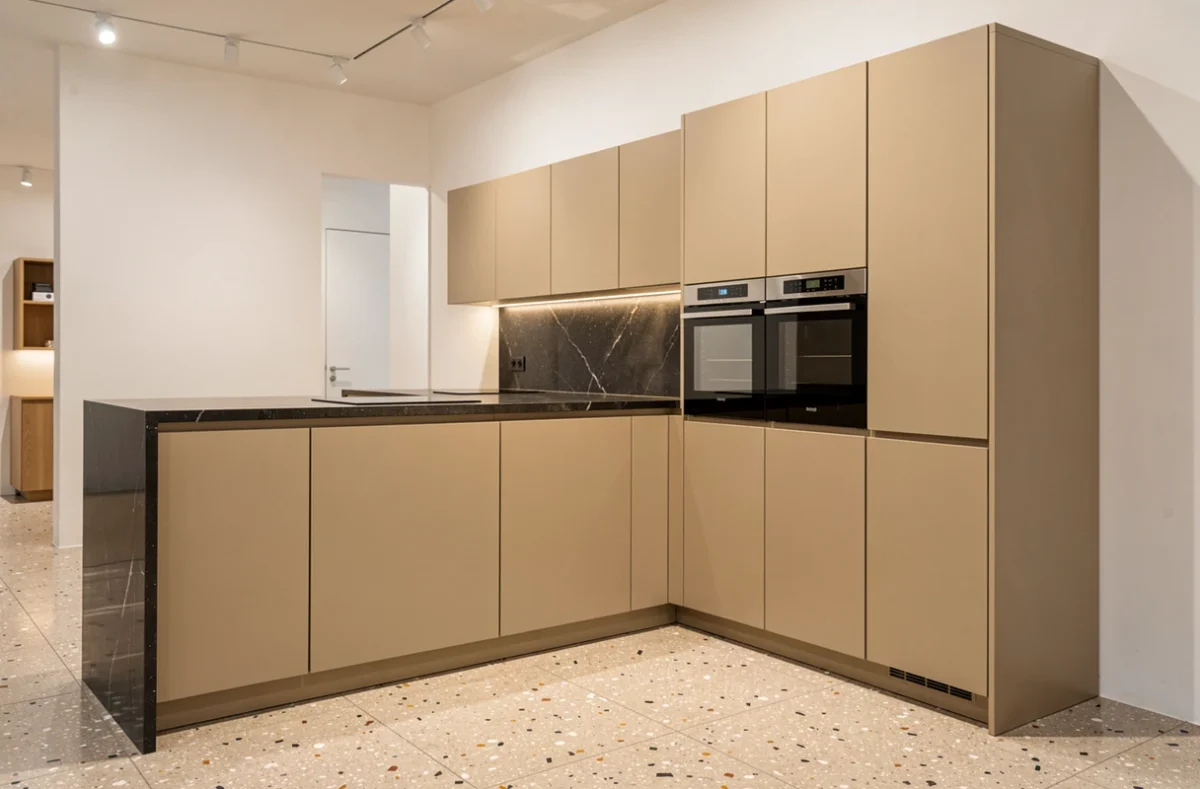 Cuisine minimaliste VAINE avec façades beige mat sans poignées et plan de travail en quartzite sombre